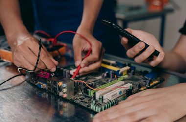 Close-up of hands working on a motherboard using electrical tools and tester.